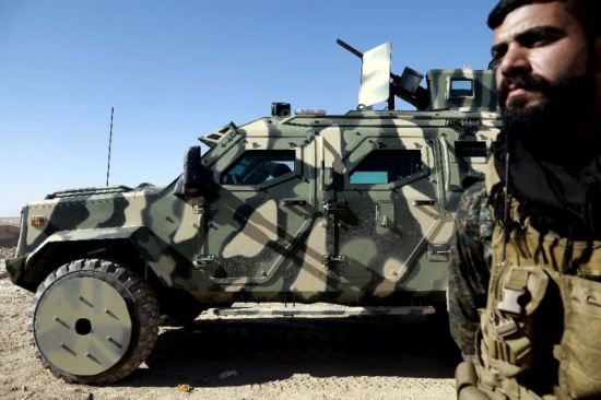 Một chiến binh của Lực lượng Dân chủ Syria đứng cạnh phương tiện chiến đấu do Mỹ cung cấp