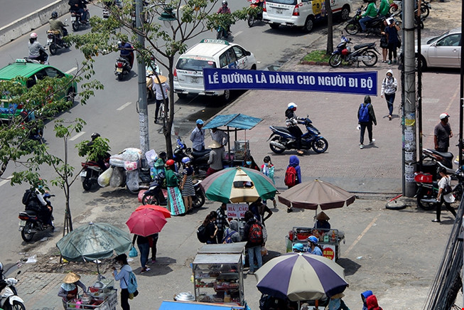 Vỉa hè đường Điện Biên Phủ, phía trước trường Đại học Hutech bị hàng chục người bán hàng rong lấn chiếm dù phía trên có treo băng rôn 