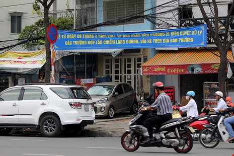 Hai ô tô, một đậu dưới lòng đường, một chắn ngang vỉa hè đường Điện Biên Phủ mặc dù phía trên có băng rôn tuyên truyền của UBND phường 21.
