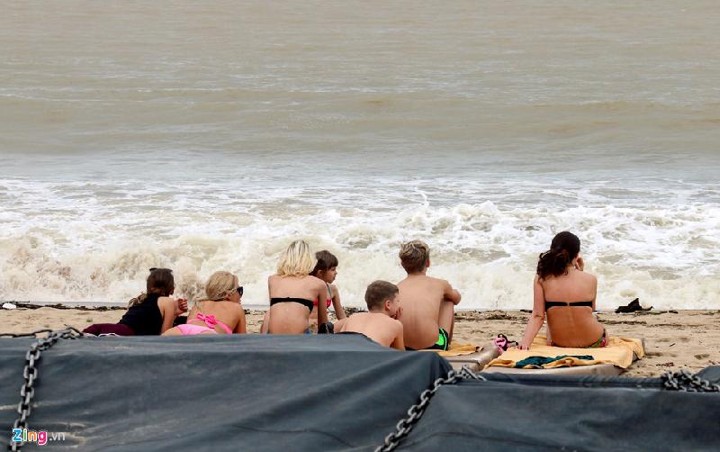 Nhiều du khách muốn tắm biển nhưng do lệnh cấm chưa được gỡ bỏ nên đành ngồi trên bãi biển.