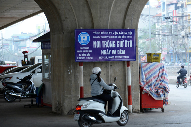 Biển trông giữ xe cắm cọc ngay dưới trụ cầu vượt, nơi không có ranh giới ngăn cách với lòng đường lưu thông các phương tiện. Tấm biển không có thông tin về giấy phép nhưng đề tên đơn vị khai thác là 
