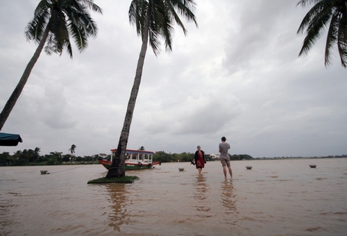 Một đôi bạn trẻ người nước ngoài băng qua con đường ngập ra phía ven sông ngắm cảnh, chụp ảnh giữa mênh mông nước.