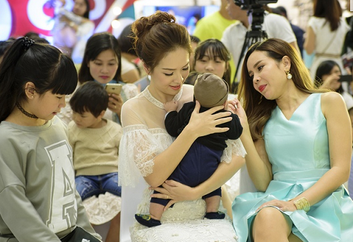 Hai nghệ sĩ chơi đùa cùng một em bé tại sự kiện.  
