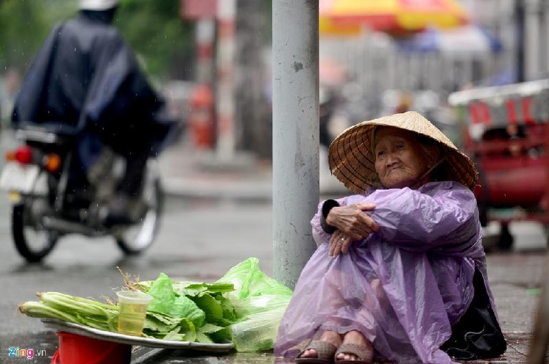 Cơn mưa rả rích không lớn nhưng cũng khiến cụ Sáu (ngụ quận 11) ngồi bán rau buồn rầu vì ế khách tại giao lộ Hàm Nghi-Pasteur, quận 1.