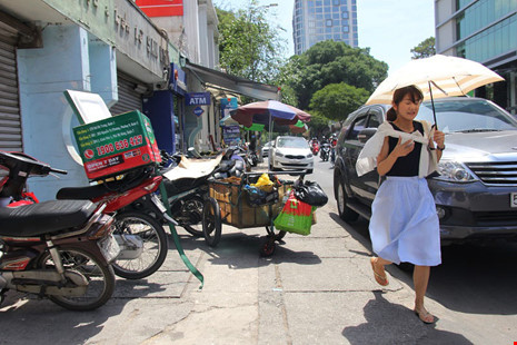 Một cô gái len lỏi qua phần vỉa hè còn sót lại do xe máy chiếm dụng và cả ô tô đậu dưới lòng đường Hai Bà Trưng.