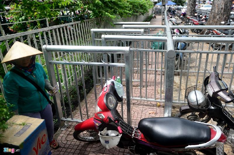 Xe máy của người đi đường dựng bít lối ra vào khiến người đi bộ phải len sát bờ rào.