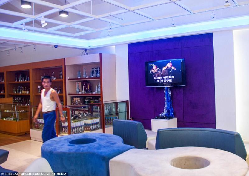 Không gian ngoài sảnh có ghế sofa êm ái và TV đang chiếu phim chiến tranh. Cạnh đó là gian hàng mỹ phẩm và rượu. 