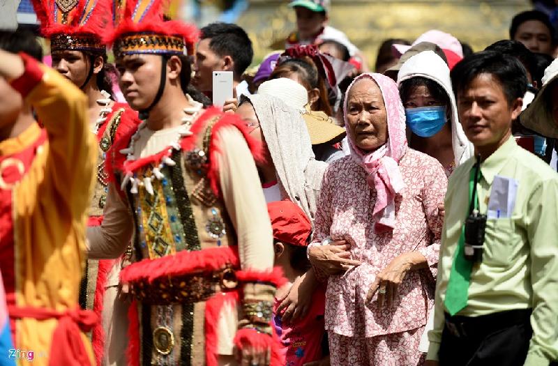 Một cụ già đội nắng cùng người thân chen chân đứng xem đoàn diễu hành, rước kiệu.